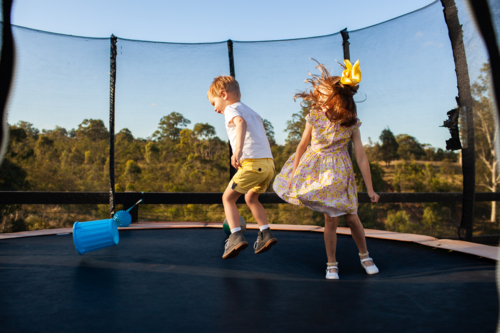 young aussie brother and sister jumping on trampoline in backyard together - Australian Stock Image