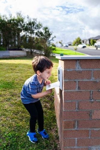 Young Aussie mixed race kid opening mailbox to collect mail - Australian Stock Image