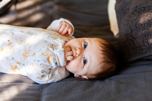 Young Australian baby lying on bed looking up with morning sunlight coming through window - Australian Stock Image