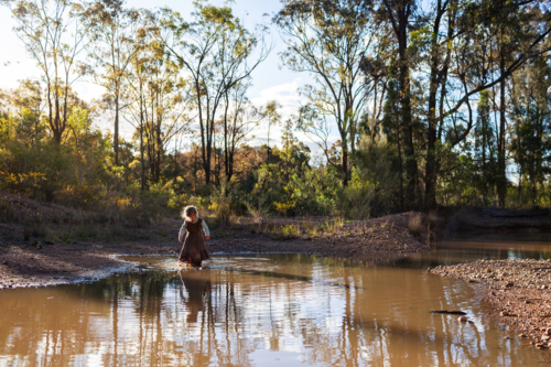 Young Australian child playing beside muddy bushland pool in rural Australia - Australian Stock Image