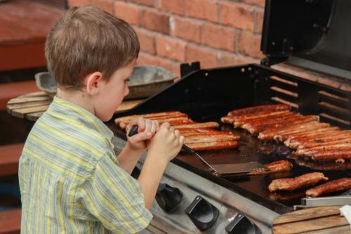 Young boy cooking sausages on the barbecue - Australian Stock Image