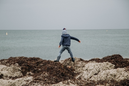 Young boy exploring coastal beach on cold winter day - Australian Stock Image