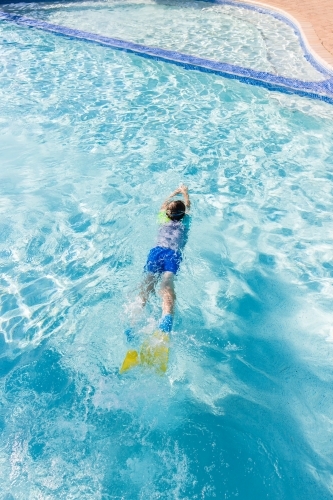 Young boy gliding in swimming pool wearing flippers - Australian Stock Image