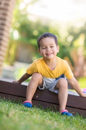 Young boy happily sitting on deck next to his eggs after easter egg hunt. - Australian Stock Image