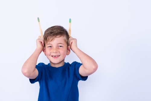 Young boy holding bamboo toothbrushes for ears - Australian Stock Image