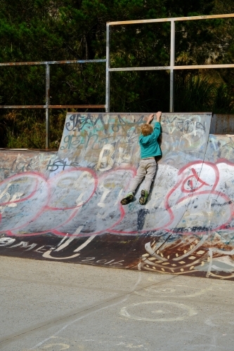 Young boy holding on to ledge in a skate park - Australian Stock Image