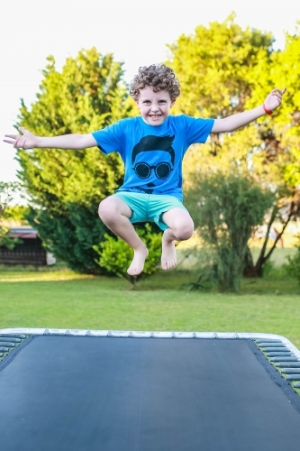 Young boy jumping on trampoline with arms flung out - Australian Stock Image