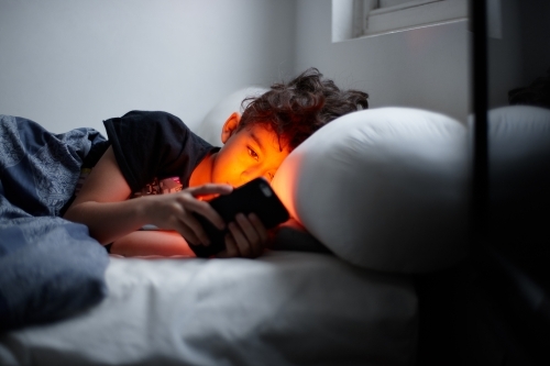 Young boy looking at device in bed