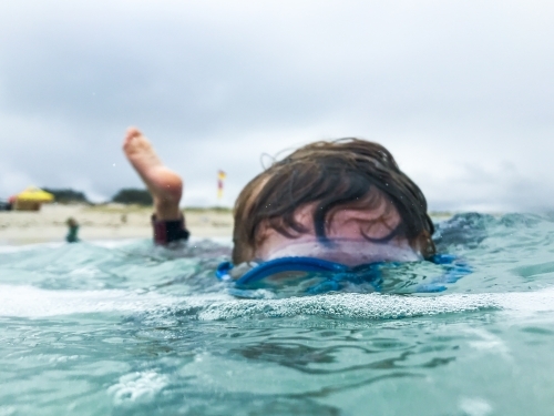 Young boy looking through mask underwater with moody sky - Australian Stock Image