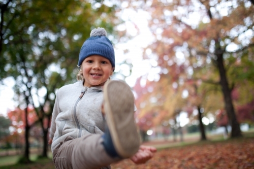 Young boy playing outdoors among piles of autumn leaves - Australian Stock Image