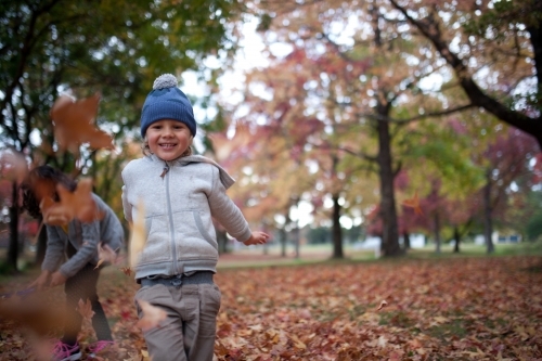 Young boy playing outdoors among piles of autumn leaves - Australian Stock Image