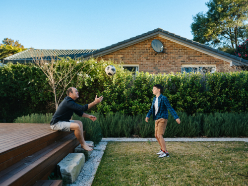 Young boy playing soccer on their garden deck with his father. - Australian Stock Image