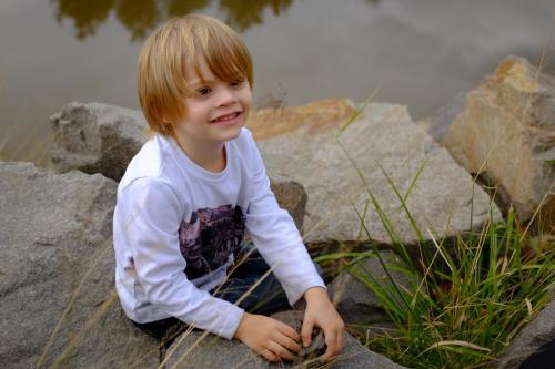 Young boy playing with rocks by the water - Australian Stock Image