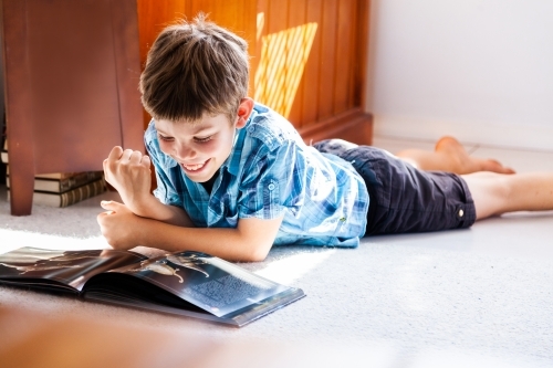 Young boy reading a book on the floor at home - Australian Stock Image