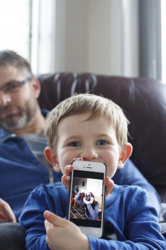 Young boy sitting on fathers lap holding phone with photo on screen