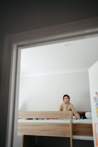 Young boy sitting on top of the bunk bed. - Australian Stock Image