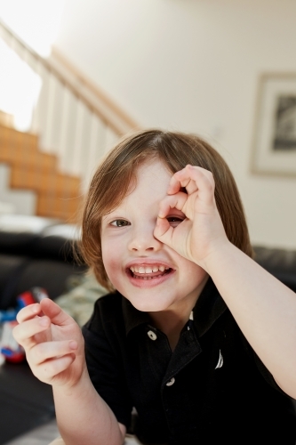 Young boy smiling peeping through his finger holes - Australian Stock Image
