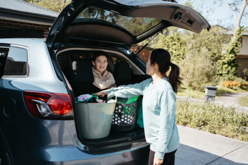 Young boy sticking his head out of the car boot with mum standing outside - Australian Stock Image