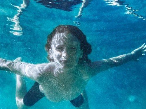 Young boy swimming underwater in blue ocean looking at camera - Australian Stock Image