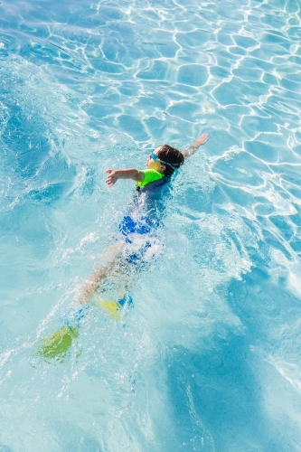 Young boy wearing googles and flippers swimming in pool
