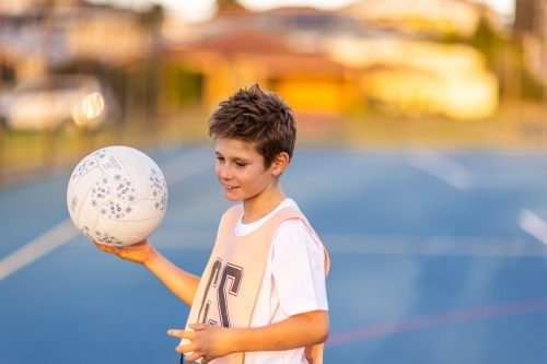 young boy wearing netball bib and holding ball on blue court - Australian Stock Image