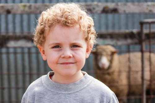 Young boy with curly hair smiling with sheep in background