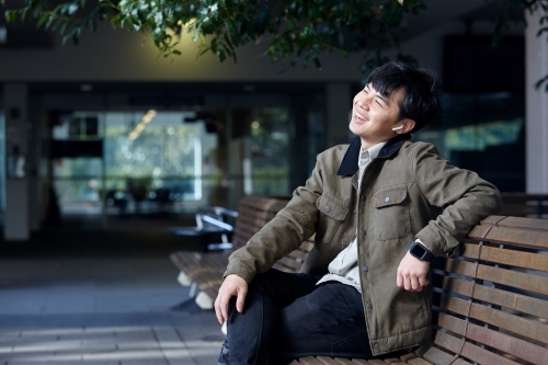 Young Chinese man smiling whilst listening to wireless headphones - Australian Stock Image