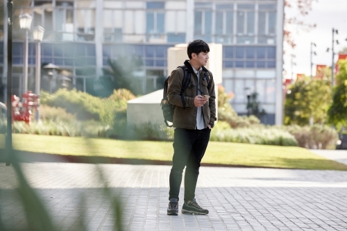 Young Chinese student outdoors with backpack and phone - Australian Stock Image