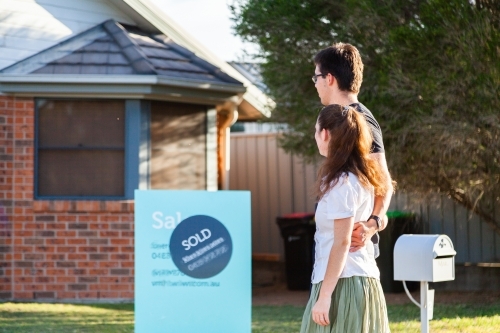 Young couple looking at front of suburban house with sold sign - Australian Stock Image