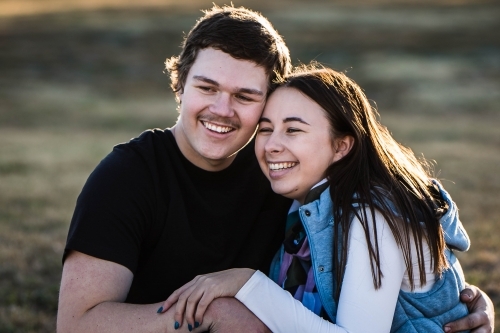 Young couple sitting close together looking into distance laughing - Australian Stock Image