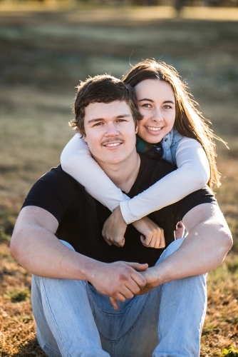 Young couple sitting on grass smiling with woman's arms wrapped around man's neck