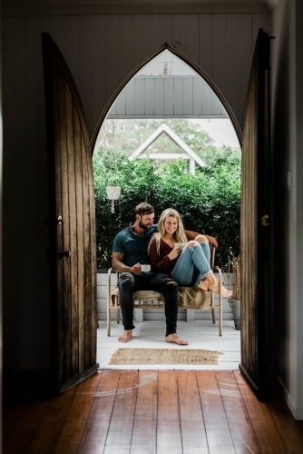 Young couple sitting outside drinking coffee on verandah - Australian Stock Image