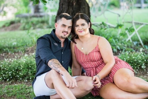 Young couple sitting together in garden touching smiling - Australian Stock Image