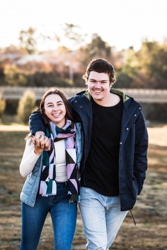 Young couple smiling and holding hands while walking - Australian Stock Image