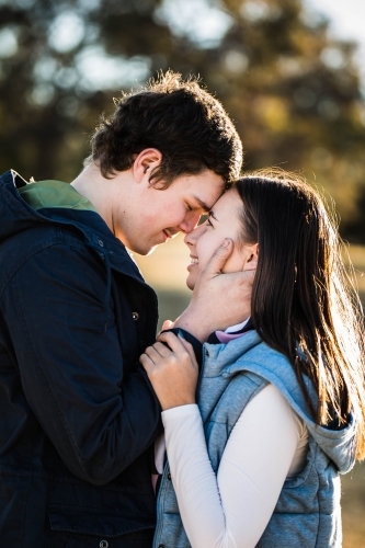 Young couple standing close together foreheads touching him touching her face smiling