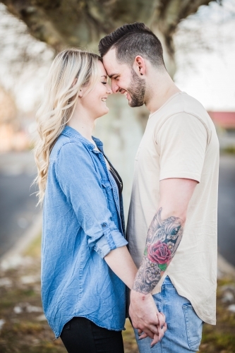 Young couple standing close together holding hands foreheads touching laughing - Australian Stock Image