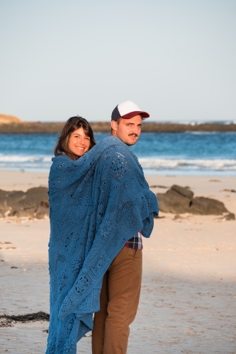 Young couple standing on the beach wrapped in a blanket.