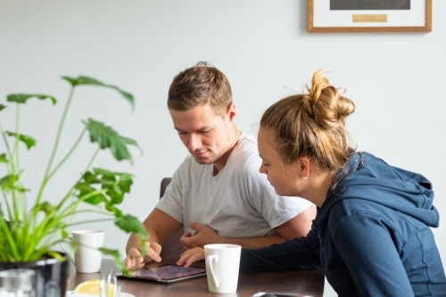 Young couple with coffee looking at tablet - Australian Stock Image