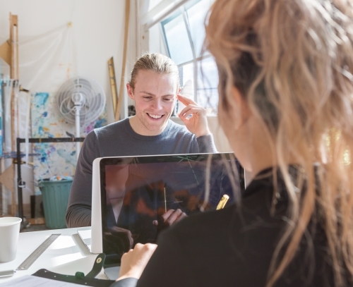 Young creative man smiling at a shared desk at work - Australian Stock Image