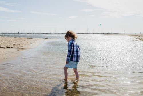 Young dressed boy walking in the ocean at St Kilda Beach, Melbourne, Victoria, Australia - Australian Stock Image