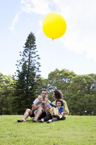 Young family of four on a hill in a park with a large yellow balloon - Australian Stock Image