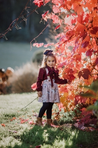 Young fashionable girl standing near autumn leavees smiling at camera - Australian Stock Image