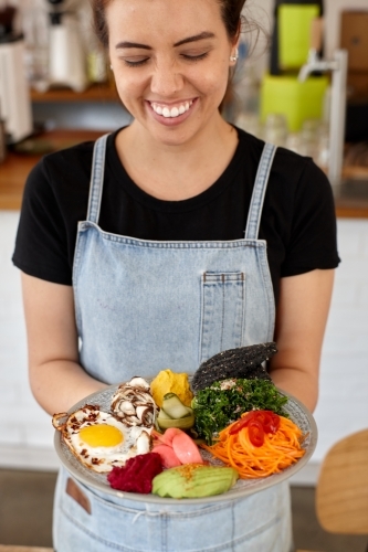 Young female cafe worker laughing holding healthy dish - Australian Stock Image