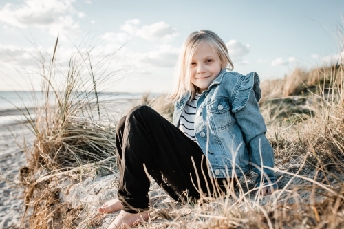 Young girl at the beach, sitting on a sand dune looking at the camera - Australian Stock Image