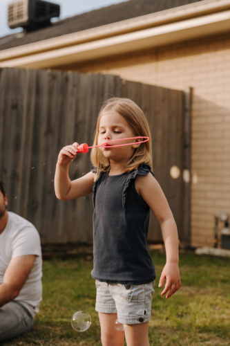 Young girl blowing with bubbles inside their yard. - Australian Stock Image