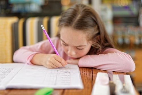 Young girl concentrating and writing in her homework book - Australian Stock Image