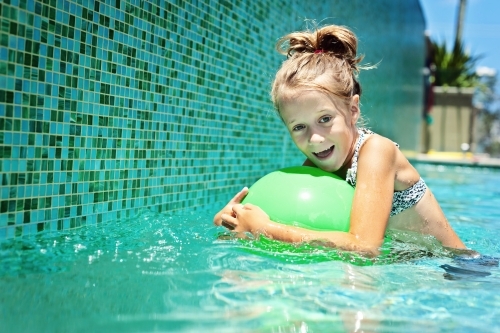 young girl floating in the pool with a green ball - Australian Stock Image