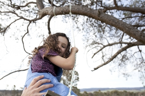 Young girl getting pushed on swing and looking down at the camera - Australian Stock Image