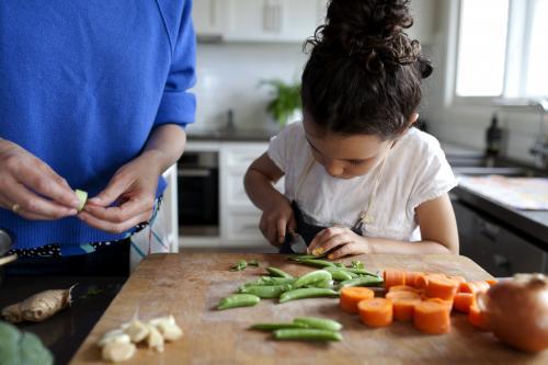 Young girl helping cook by chopping vegetables - Australian Stock Image