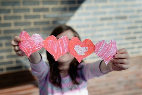 With a loving heart - Young girl holding a hand made card of connected paper love hearts - Australian Stock Image